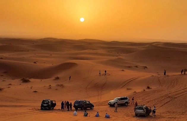 4x4 vehicle parked on dune with travelers watching sunrise in Merzouga