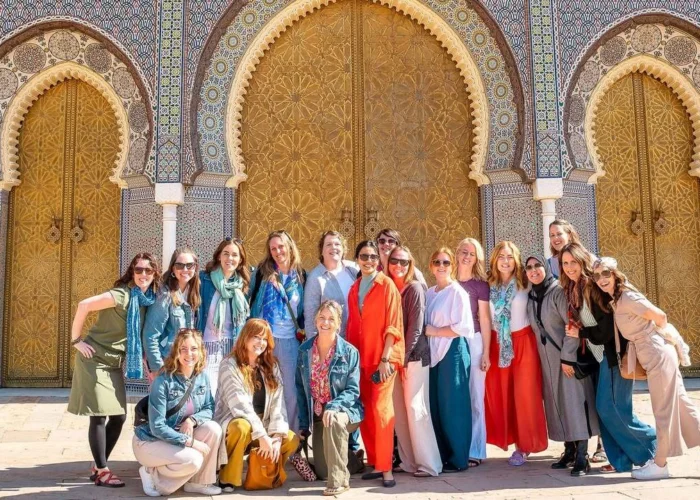 Group of travelers on a 7 days tour in Morocco posing in front of ornate Moroccan palace doors with zellige tilework