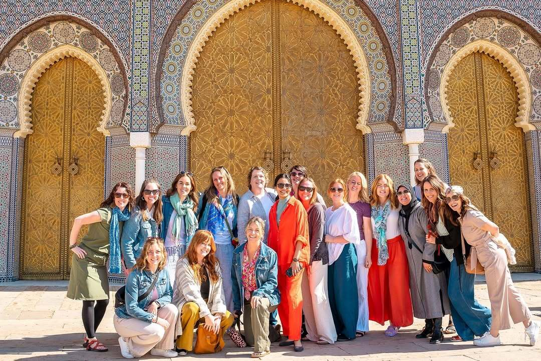 Group of travelers on a 7 days tour in Morocco posing in front of ornate Moroccan palace doors with zellige tilework